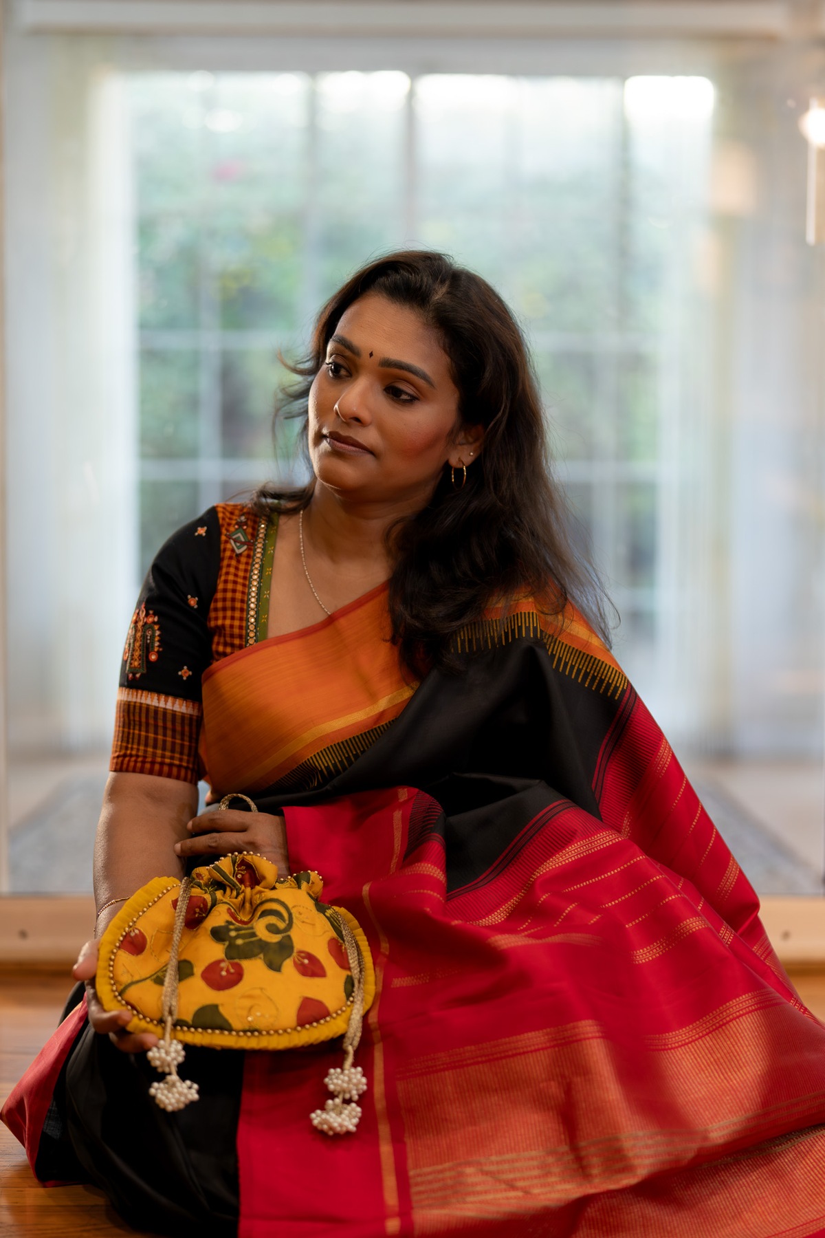 Subha showcasing a yellow potli with her black and red saree